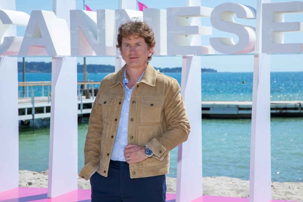 해변가에 설치된 Cannes 간판 앞에 서 있는 토드 하워드.