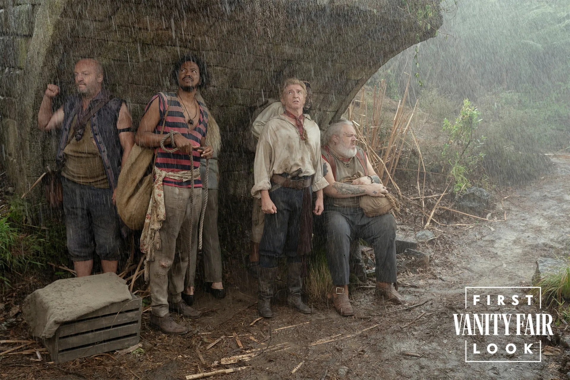 The crew of Our Flag Means Death Season 2 standing under a covering in the rain.