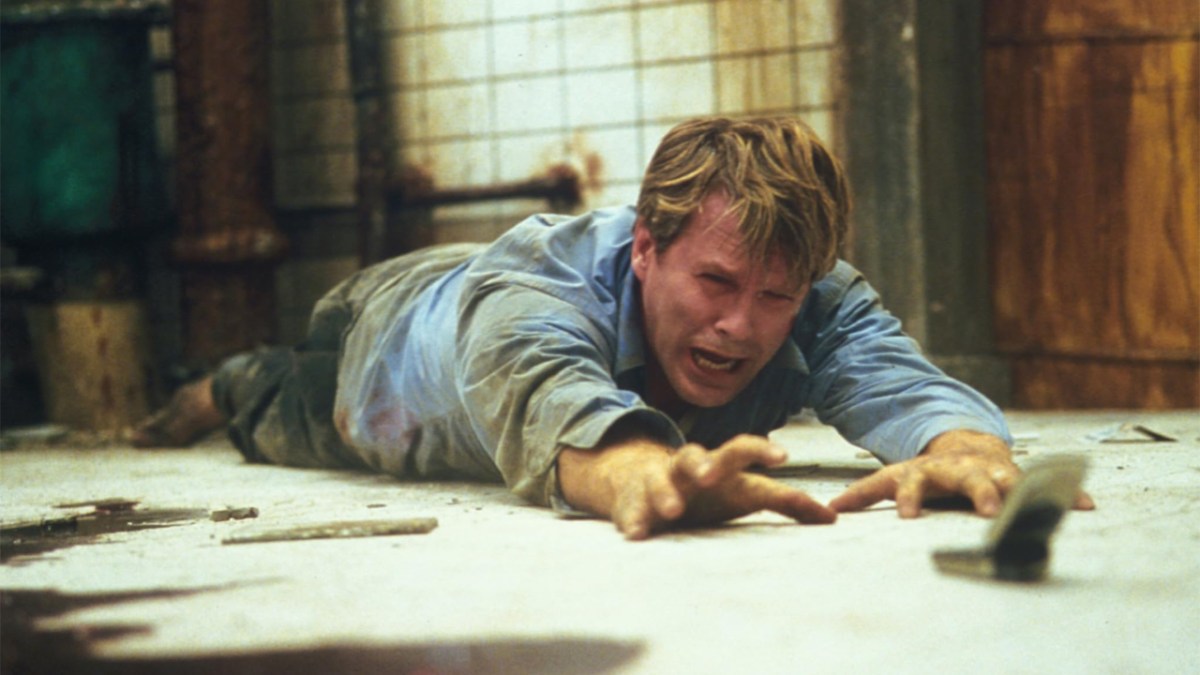 Cary Elwes, alcanzando un teléfono mientras está en el suelo con una mirada torturada en su rostro, tomado de la primera película de Saw.