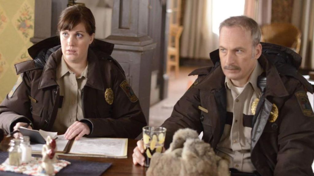 Deputy Molly Solverson sits next to Police Chief Bill Oswalt. This image is part of an article about all major cast members and actors in Fargo Season 5.