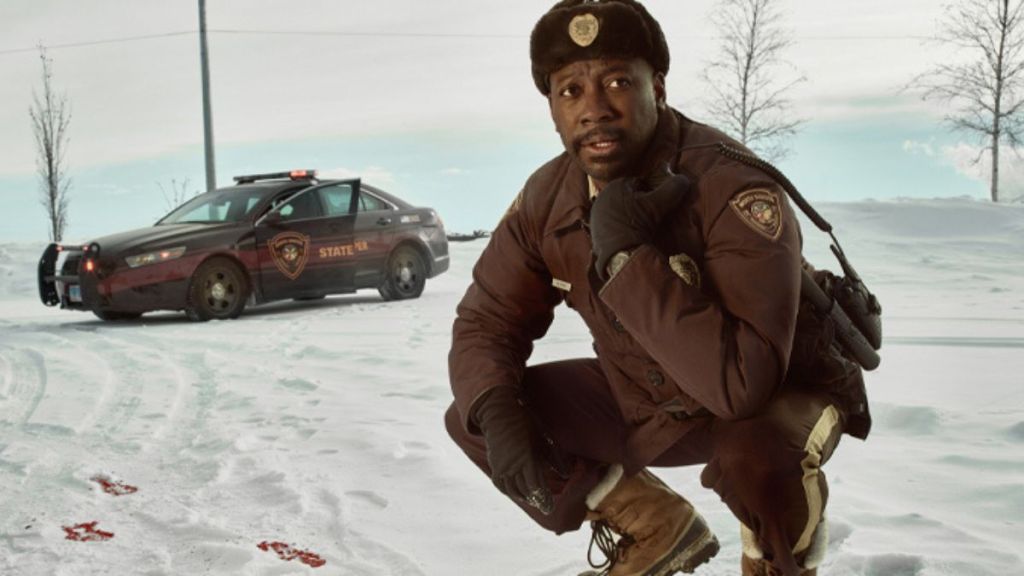 Witt calls on his radio while tracking bloody footprints in the snow. This image is part of an article about all major cast members and actors in Fargo Season 5.