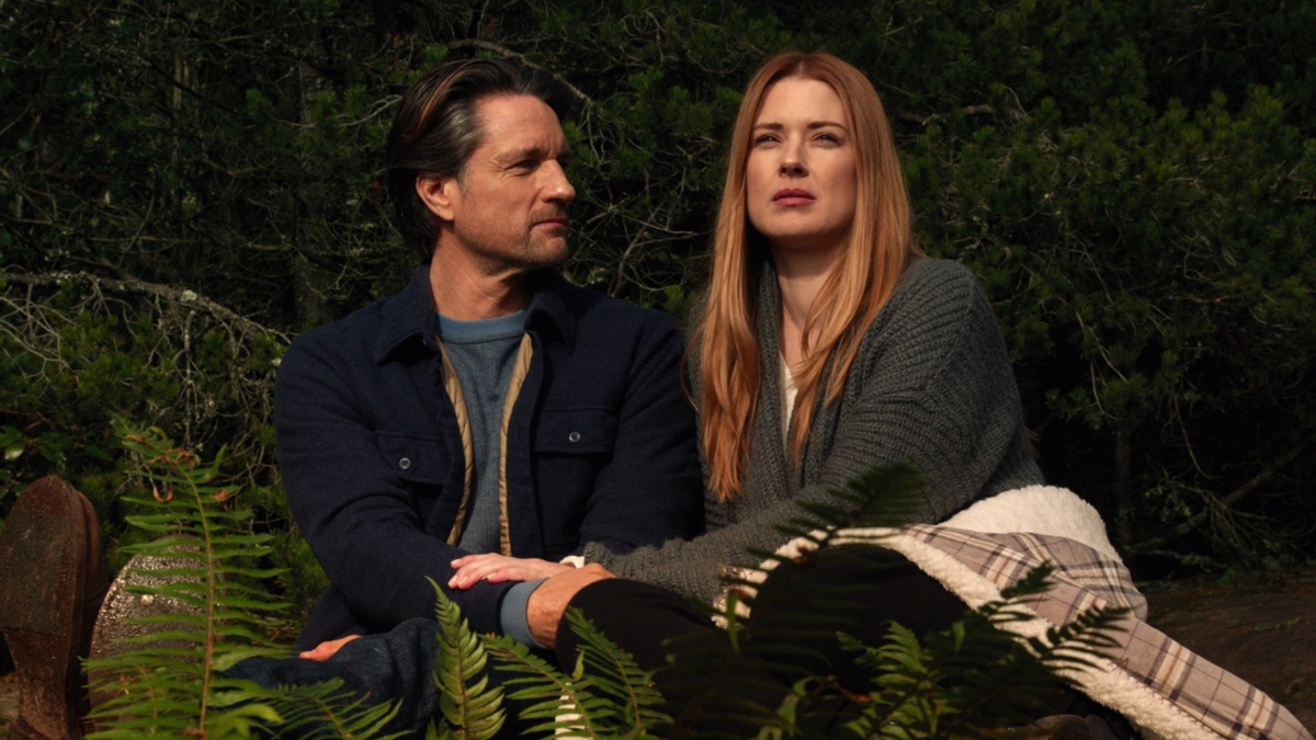 Two characters sitting in a forest. This image is part of an article about when Virgin River Season 6 comes out.