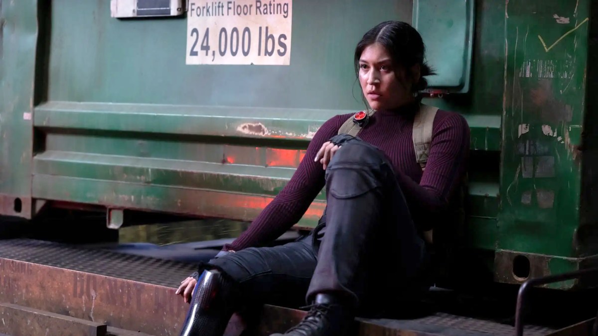 Alaqua Cox as Echo in the character's titular show. The image shows her sitting on some metal grating beside a sign noting a forklift's floor rating.
