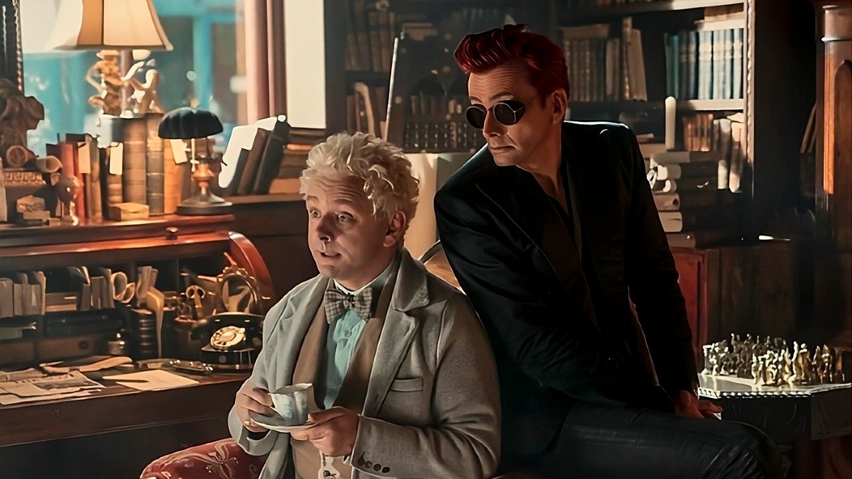 Aziraphale drinking tea in his bookshop while Crowley leans over his shoulder in a still from Good Omens 2.