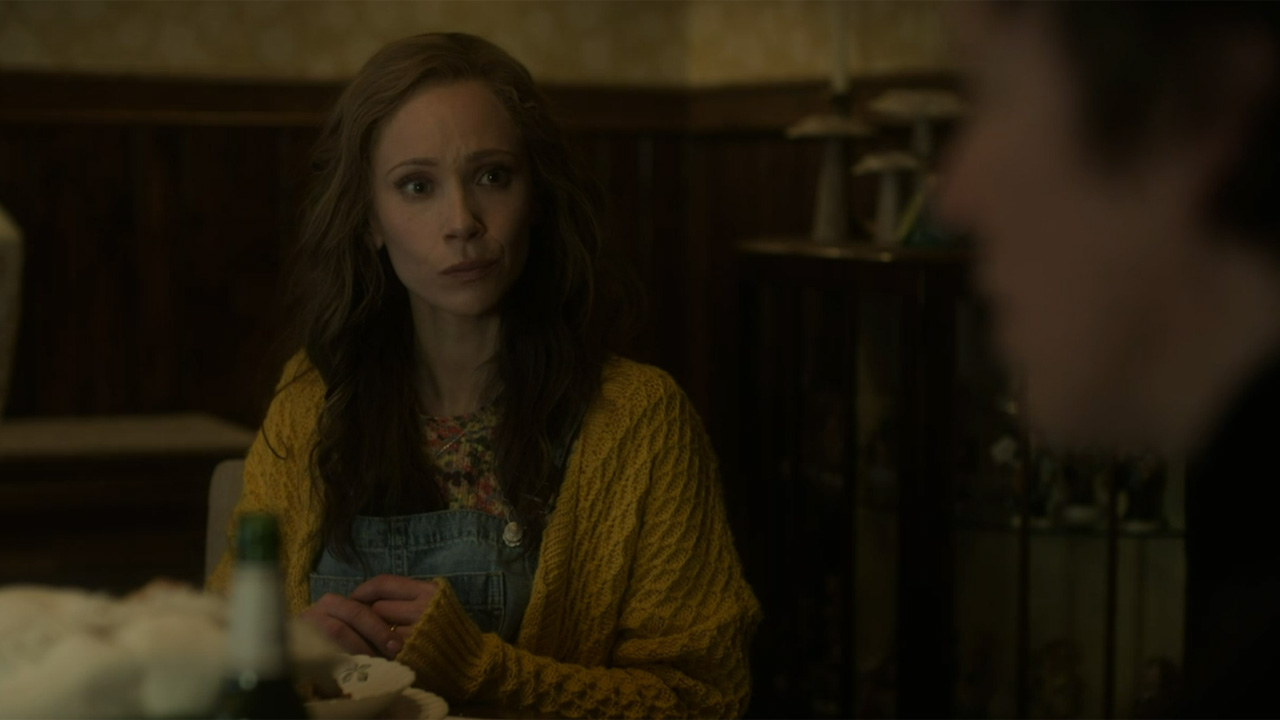A woman in yellow sitting at a table, with another man in the foreground. 