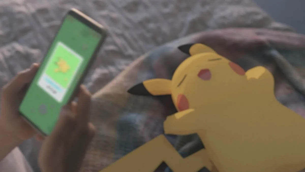 An image of a sleepy Pikachu, with a person holding up a phone using the Pokemon Sleep app. This image is part of an article about all the Shiny Pokemon in Pokemon Sleep and how to catch them. 