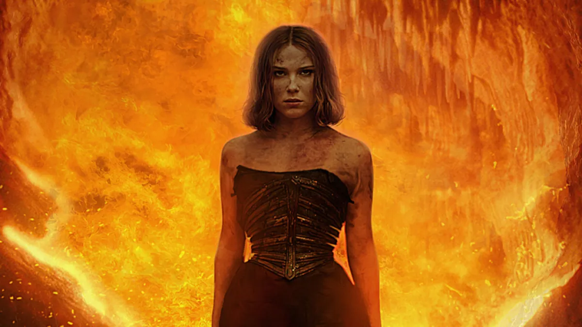 A woman standing in front of a wall of flame. This image is part of an article about Netflix's Damsel Ending, Explained.