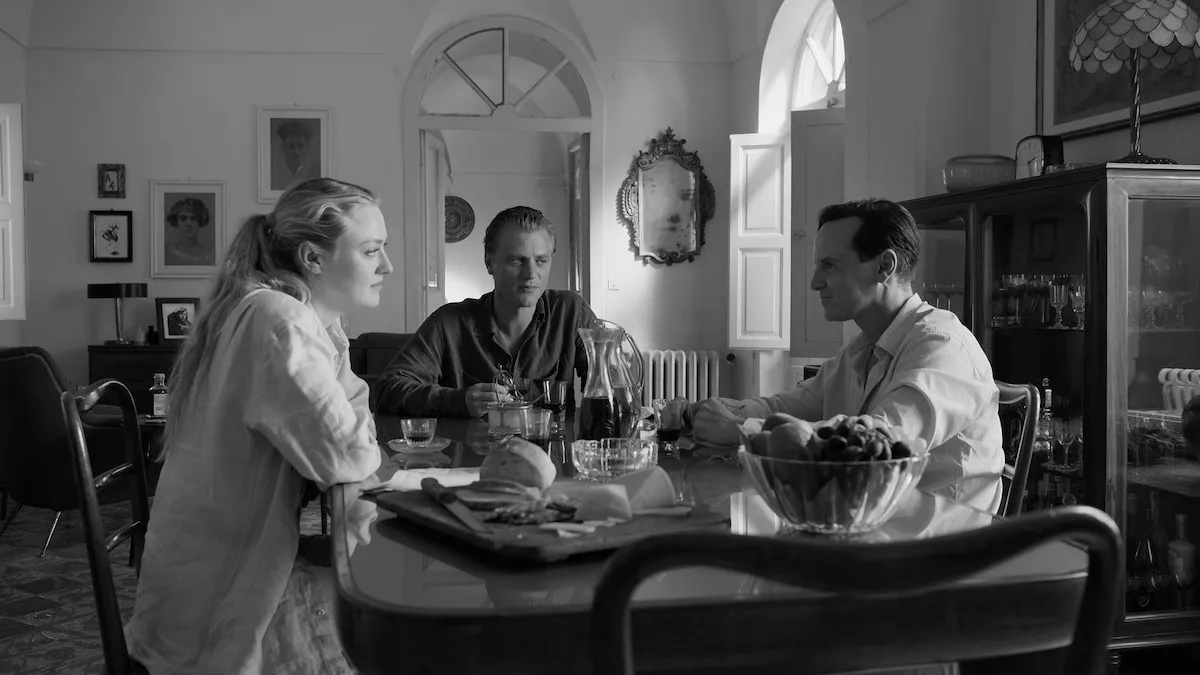 A black and white image of three people, a woman and two men, sitting around a table. This image is part of an article about all major actors and case members for Netflix's Ripley.