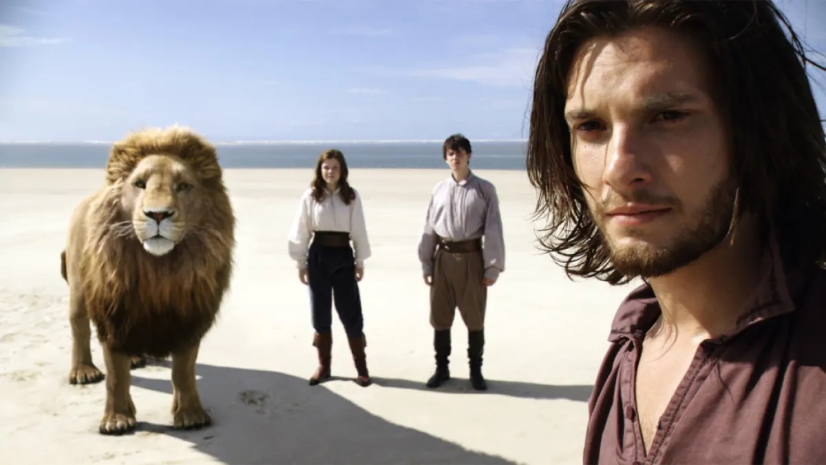 A Lion and three people standing on a beach in Voyage of the Dawn Treader.
