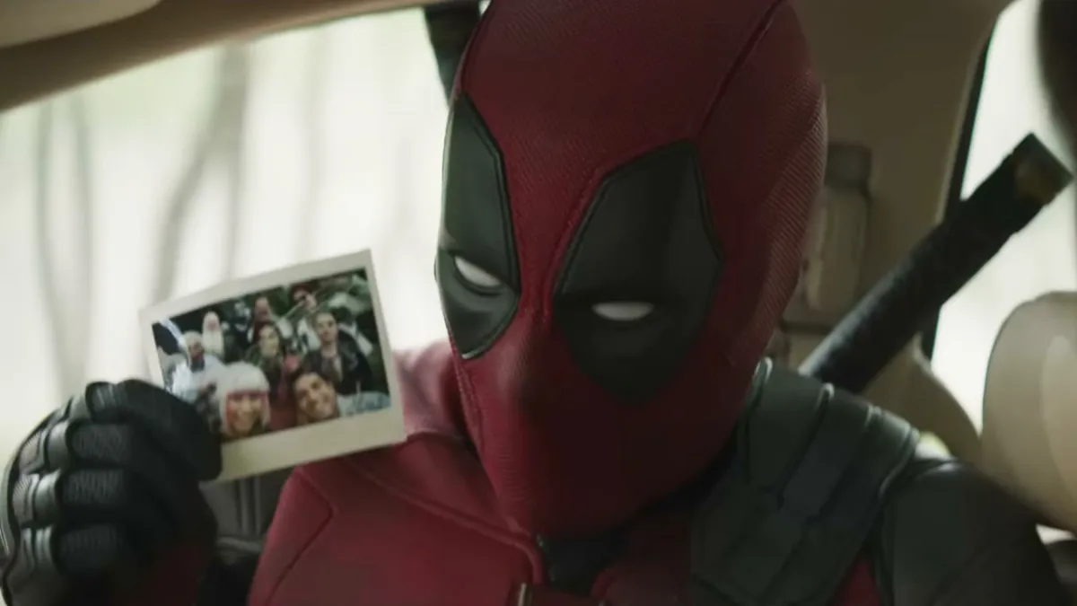 Deadpool in Deadpool & Wolverine, a red-suited superhero, holding up a photograph.