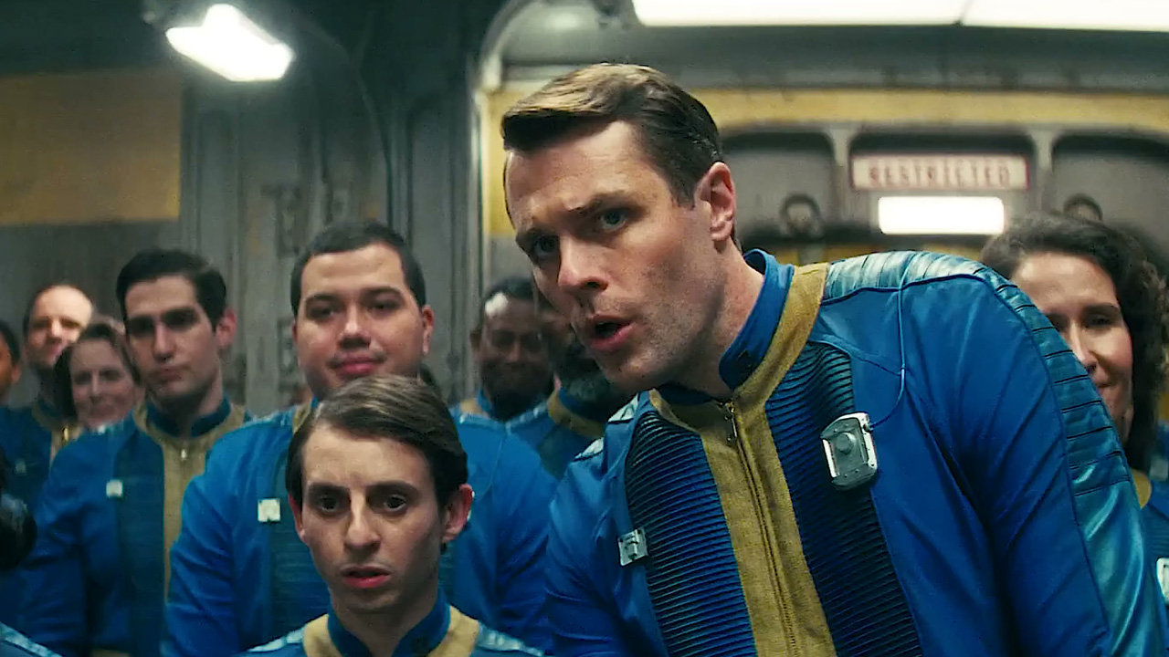 The Fallout TV show, in a Vault, with one blue jumpsuit wearing character leaning over to talk to another.