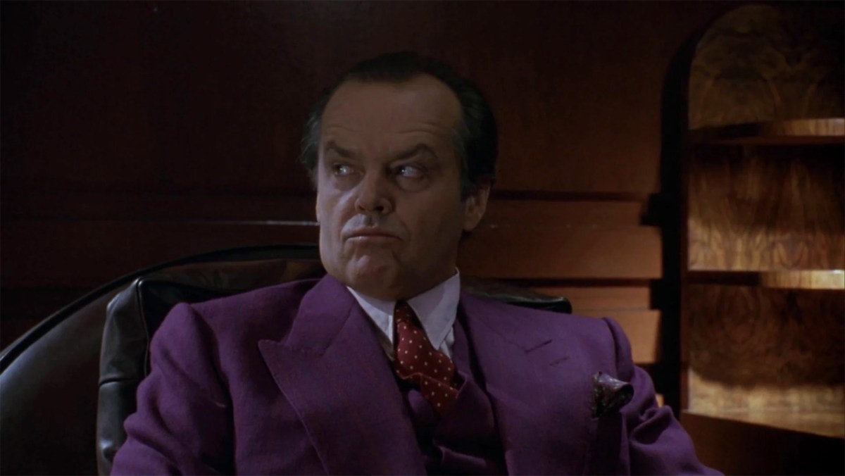 Jack Nicholson, como Jack Napier en la película Batman de 1989, vestido con un traje morado.  Esta imagen es parte de un artículo sobre cuál es el origen del comodín en los cómics de Batman.