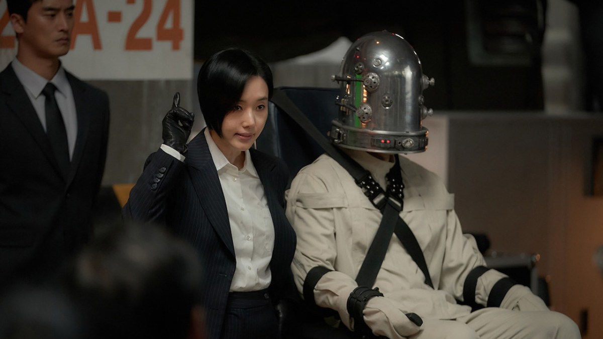 Parasyte: The Grey, with a woman and a man in suits, and a person with a metal helmet strapped into a chair. This image is part of an article about whether Netflix's Parasyte: The Grey is based on the manga or anime.