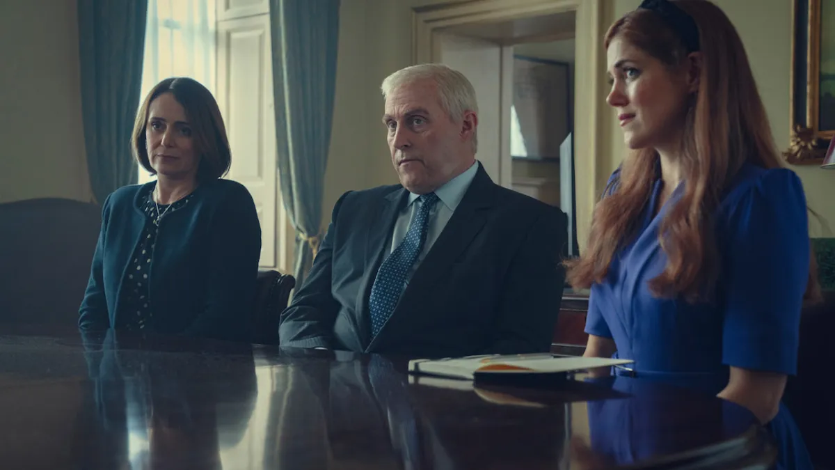 Three members of the cast of Scoop sitting at a table, one resembling Prince Andrew.