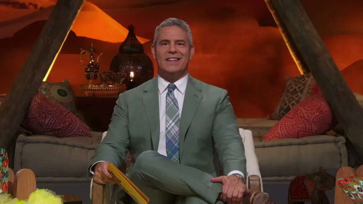 Andy Cohen, sitting in a chair in a grey suit.
