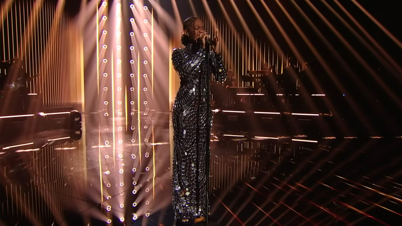 American Idol winner Just Sam singing on stage in a silver shimmering dress.
