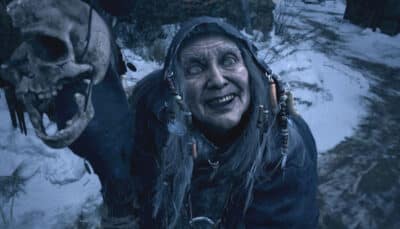 A creepy figure with a hood and weathered face, grinning in a snowy setting