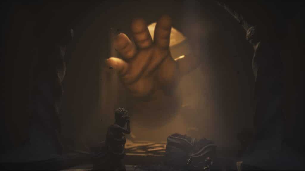 A massive hand reaches toward Alone and Low in a dark tunnel in Little Nightmares 3