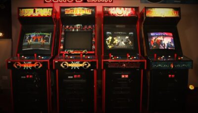 Row of classic Mortal Kombat arcade machines, including Mortal Kombat 1, 2, 3, and 4, displayed side by side in a dimly lit arcade.
