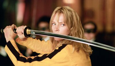 A woman in a yellow tracksuit holds a katana in a fighting stance during an intense scene from the film Kill Bill