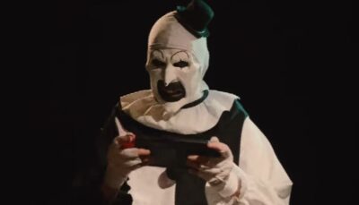 Art the Clown intensely playing a handheld gaming console in a dark scene