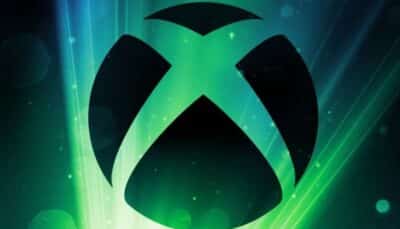 A large black Xbox logo glowing with bright green and blue light beams on a dark background
