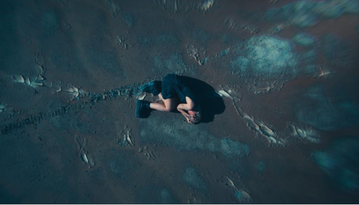 A lone person lies curled on a desolate surface in Sleep Awake