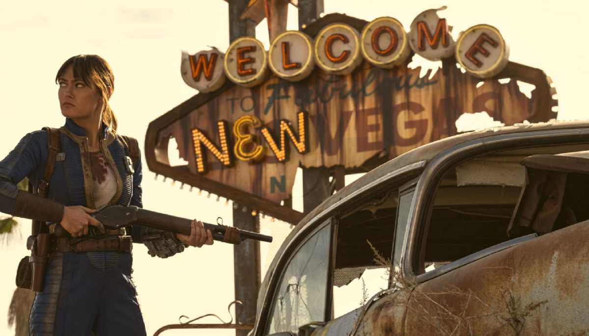 Lucy from Amazon’s Fallout series standing armed beside the ruined Welcome to New Vegas sign, capturing fan concerns over Season 2 accuracy.