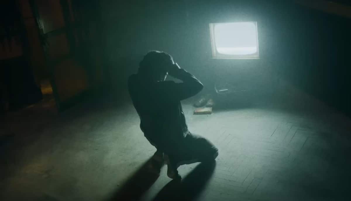 A man collapses on the floor of an empty room lit by a flickering television in Silent Hill