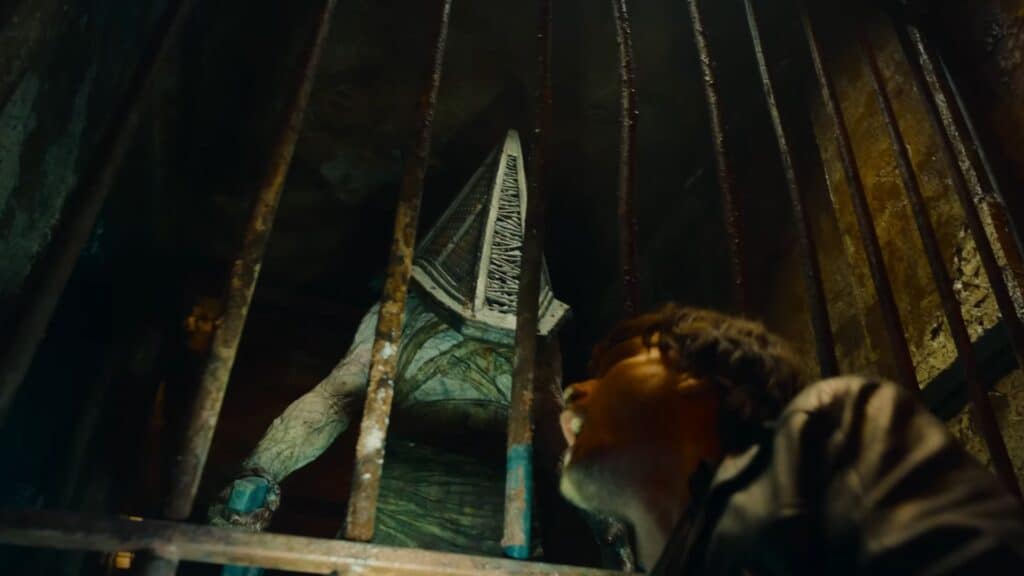 A horrifying humanoid monster stands behind metal bars as a man recoils in fear in Silent Hill