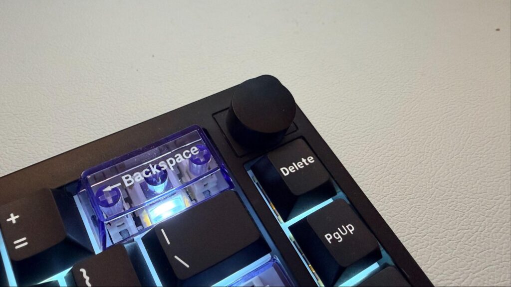Close-up of the EPOMAKER Magcore65 Lite keyboard showing the transparent Backspace key, volume knob, and compact 65% layout designed for portable home and travel use.