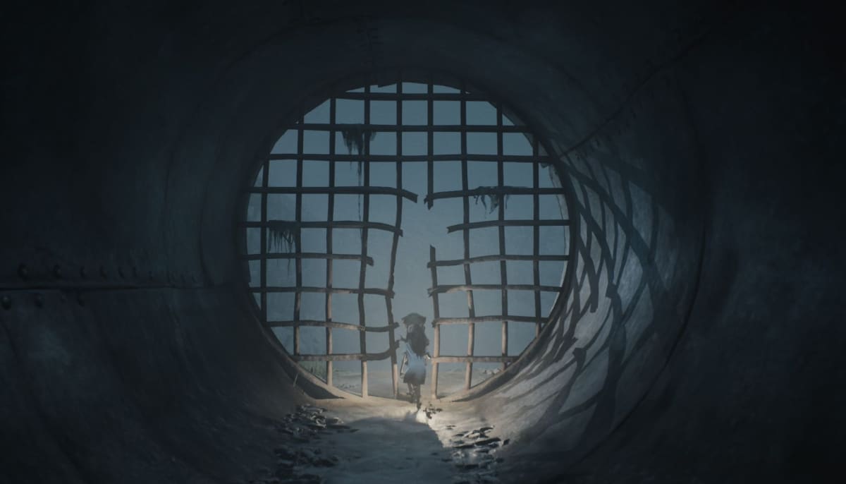 Brother and sister protagonists stand inside a dark tunnel facing a broken metal gate on their escape from the island in Reanimal horror game.