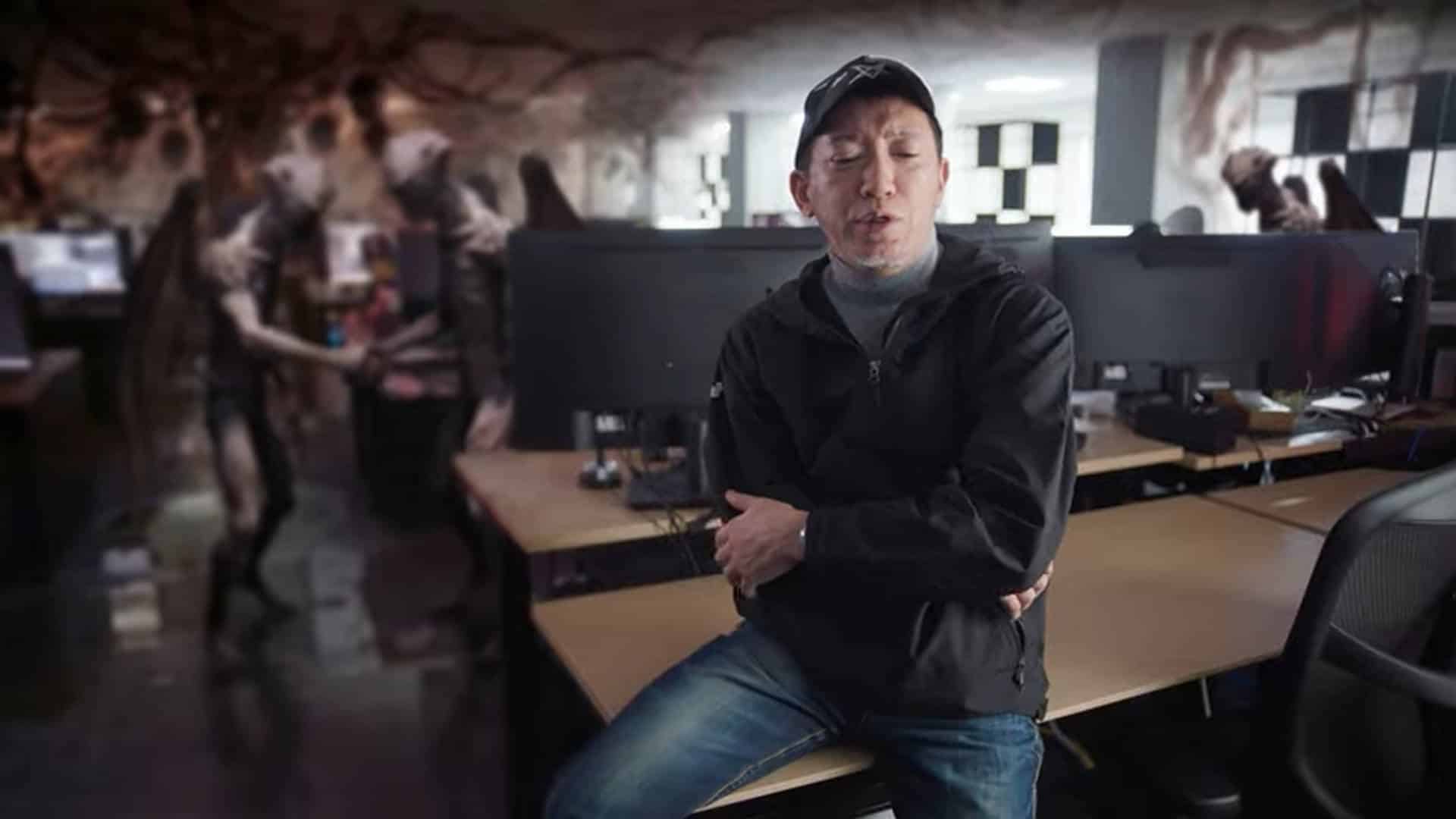 Shift Up developer sat in an interview qwith green screen demons behind him in an office setting.